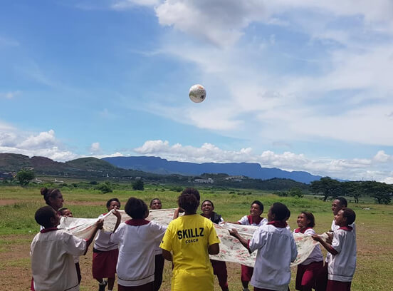 Young people play football with mountains in the distance 