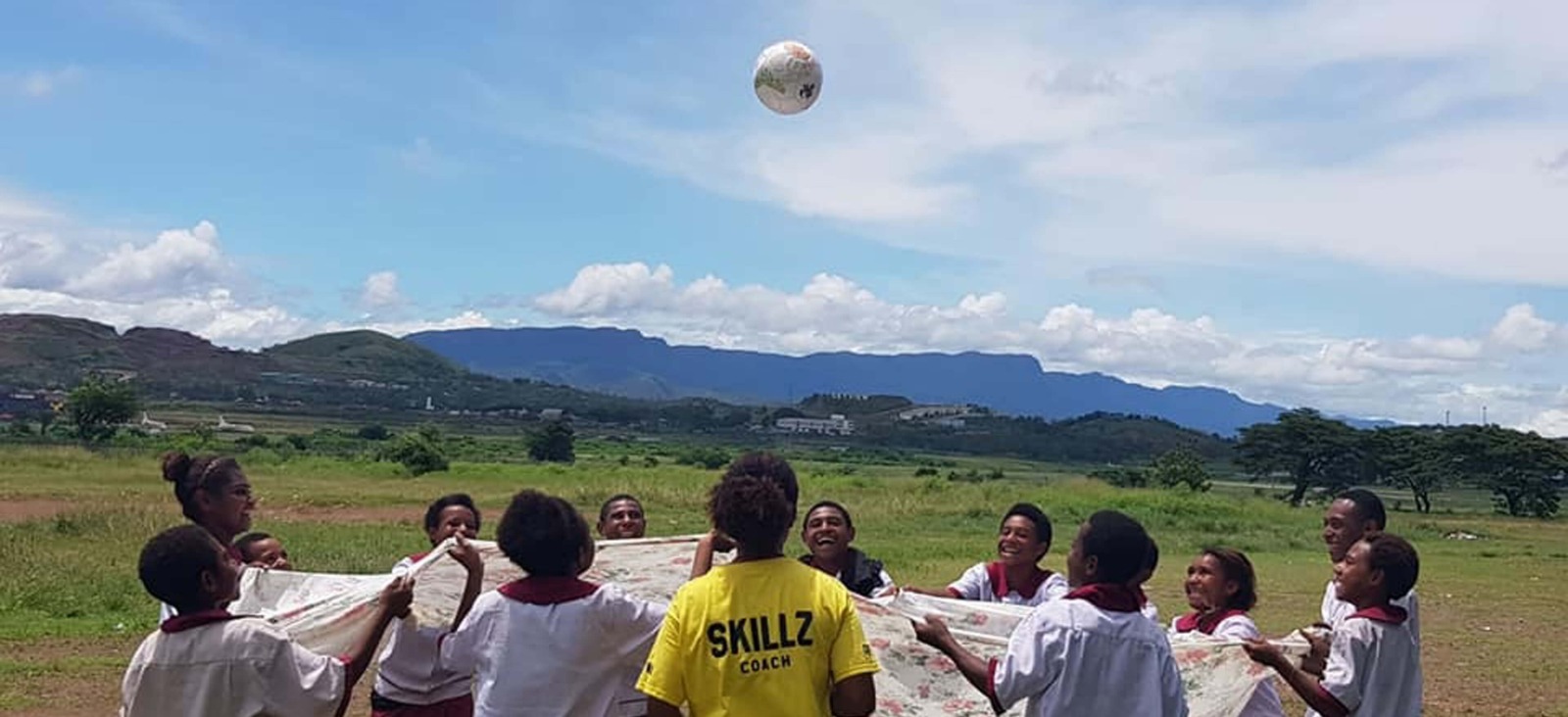 Young people play football with mountains in the distance