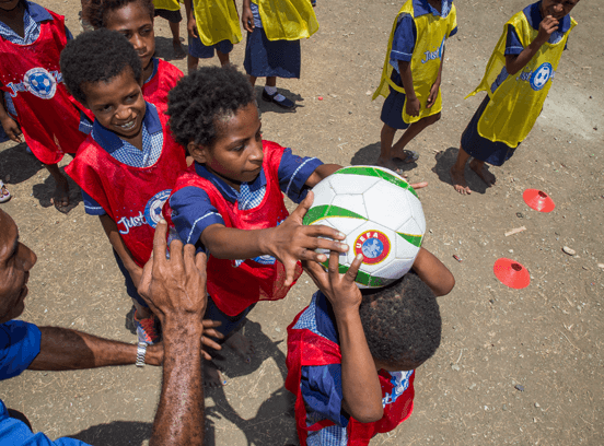 Small children pass a football over their heads 