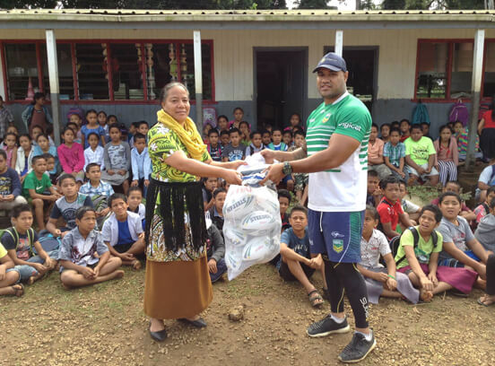 Young children wait for volunteer leaders to pass out rugby league footballs 