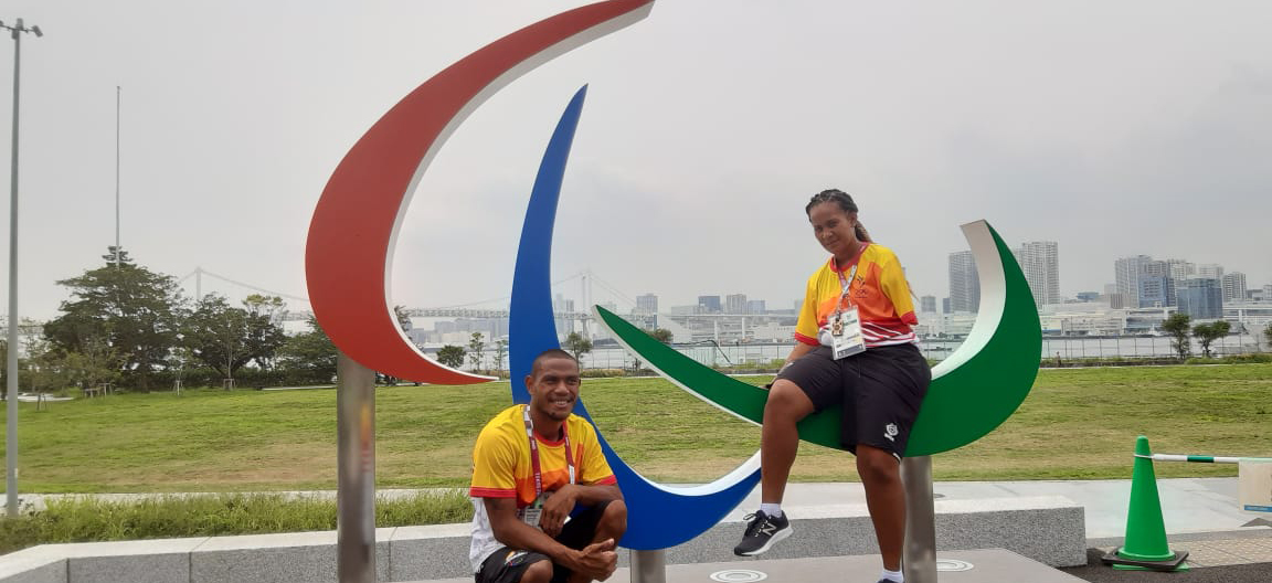 Two athletes sitting on a statue of the Paralympic logo