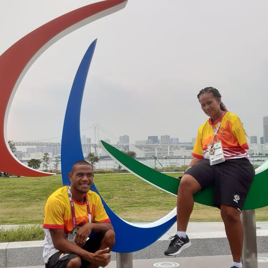 Two athletes sitting on a statue of the Paralympic logo