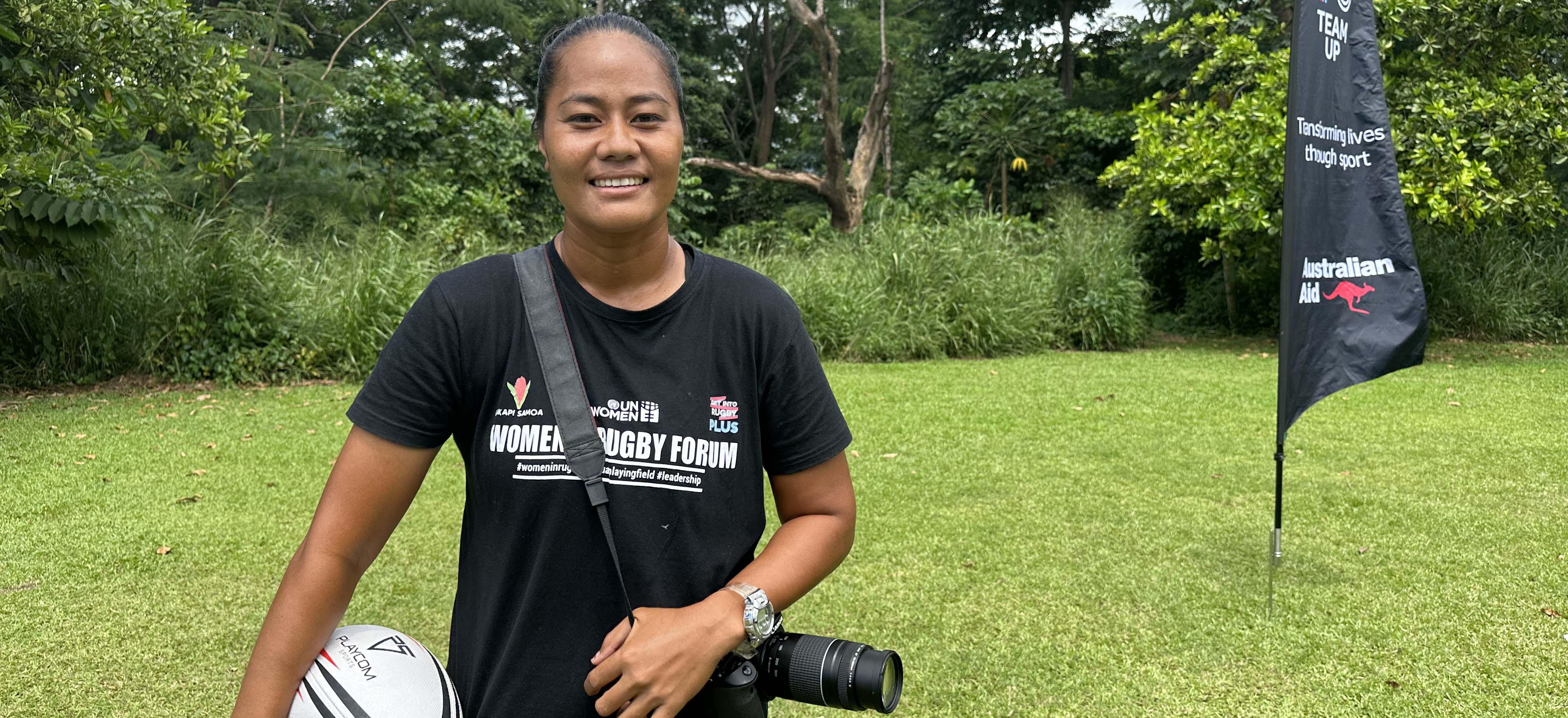 A woman in Samoa holding a rugby ball and a camera