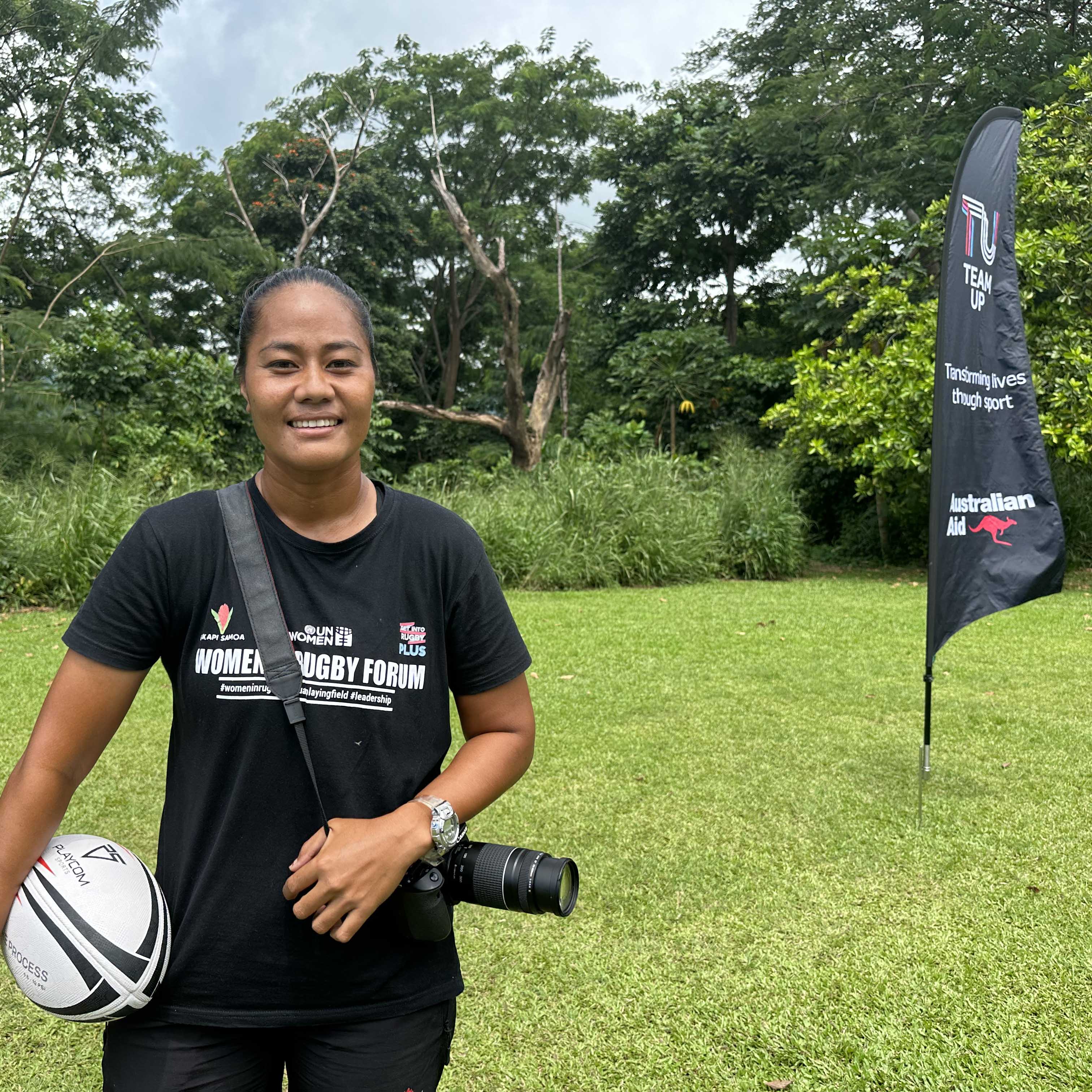 A woman in Samoa holding a rugby ball and a camera