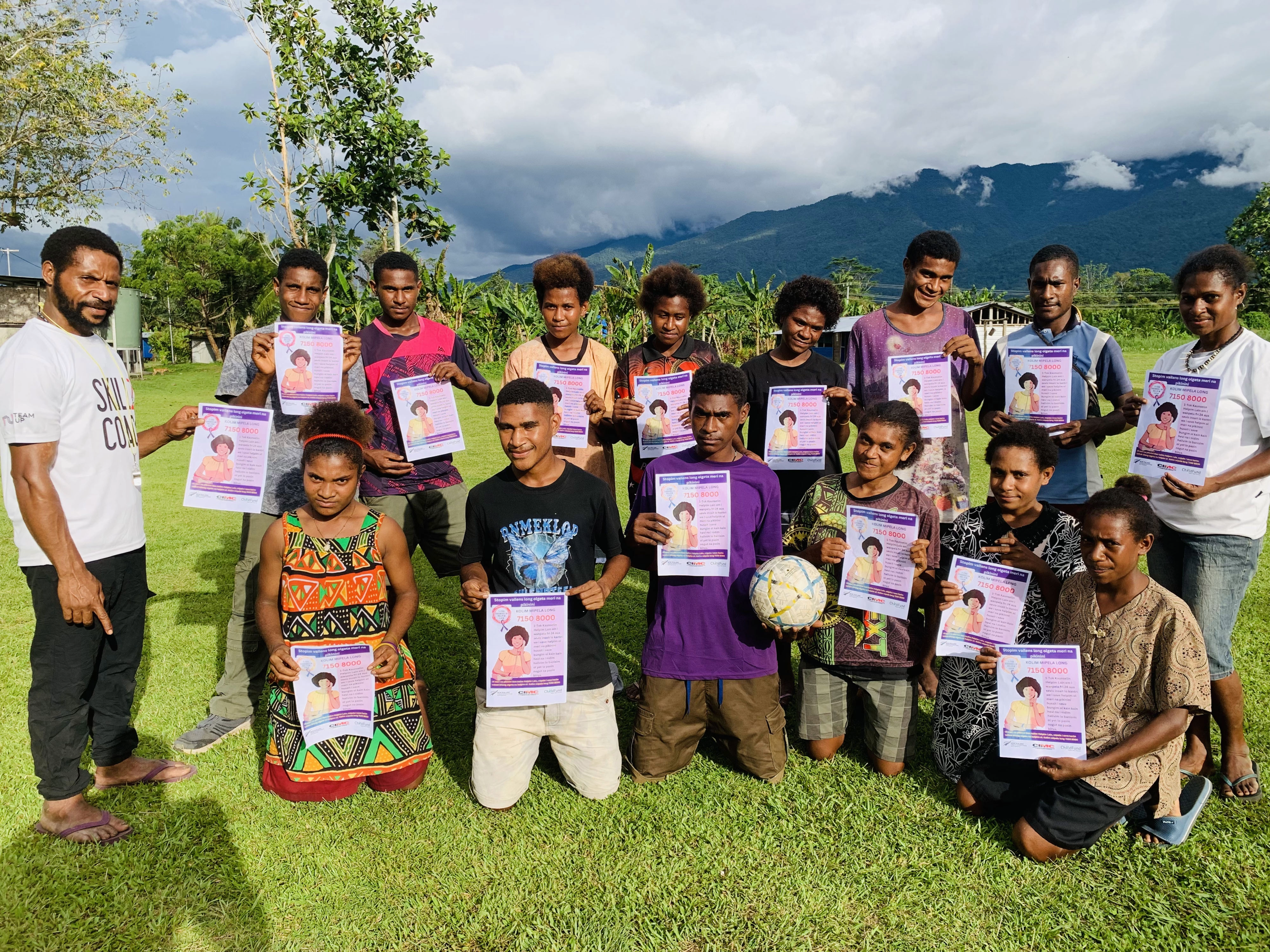 A group shot of K4K participants on the field holding up an informational poster on gender-based violence