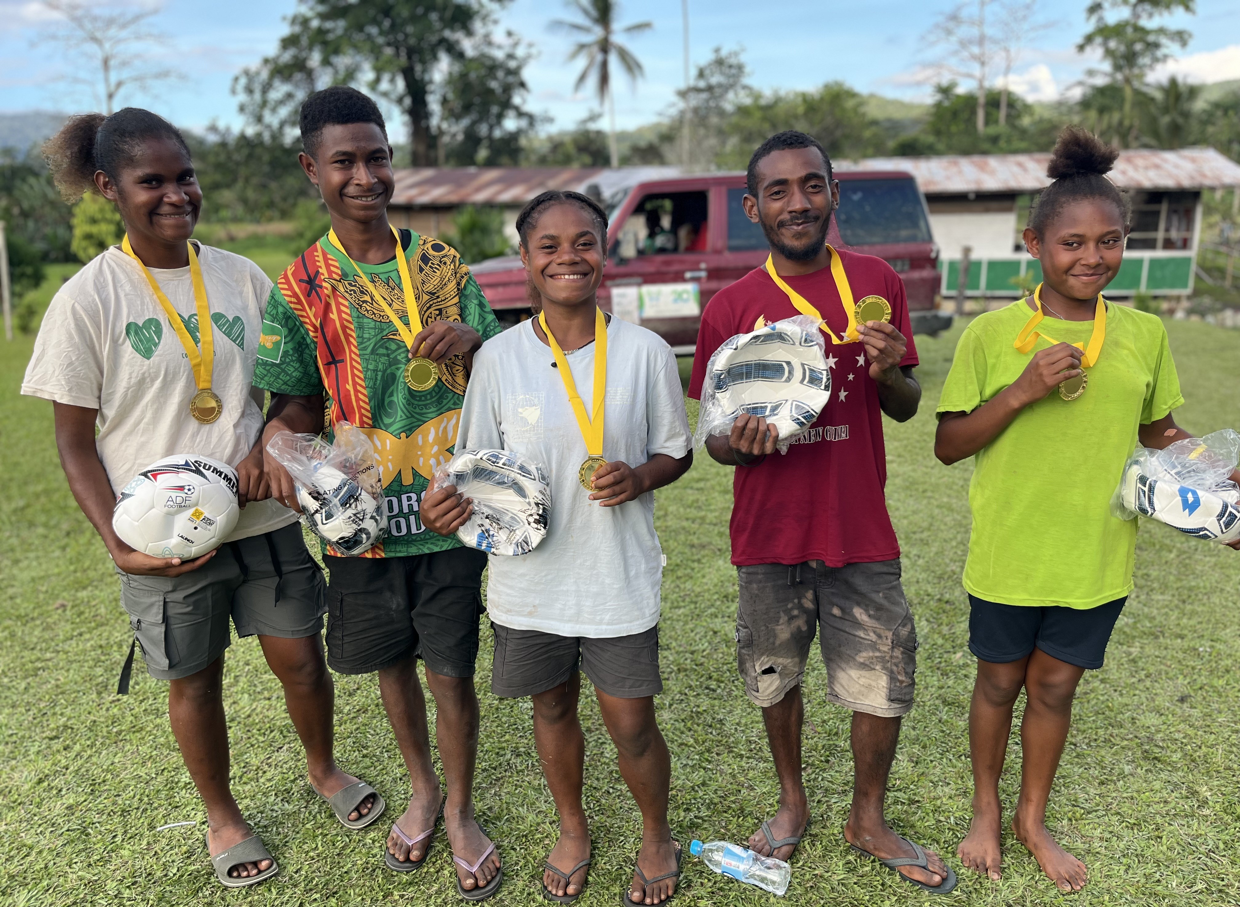  IMG_1625.jpeg: A group shot of five K4K participants, smiling at the camera, wearing medals and holding soccer balls gifted as prizes for winning the tournament